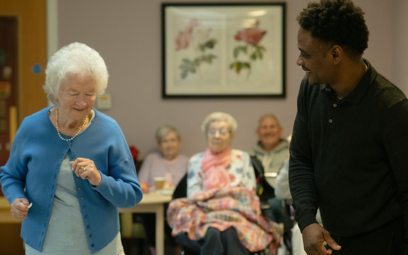 Elderly woman dances with caregiver in a community room by Age Cymru courtesy of Unsplash.