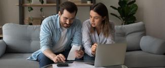 A couple sitting on a couch working on a laptop together.